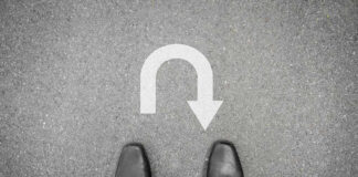 Feet in black shoes facing U-turn road marking.