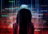 Hooded figure with cybersecurity terms and binary code background.