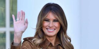 Melania Trump waving and smiling while wearing a stylish coat