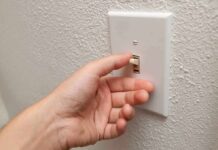 A hand reaching to turn on a light switch on a textured wall