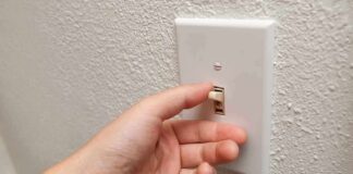 A hand reaching to turn on a light switch on a textured wall