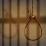 A noose hanging in front of prison bars, casting shadows