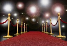 A red carpet lined with gold stanchions and ropes under bright spotlights