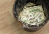 A trash can filled with crumpled hundred dollar bills