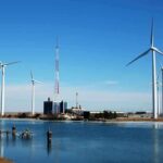 GREEN Energy Destroying Amazon — HORRIFYING DISCOVERY Wind turbines and a communication tower near a body of water under a clear blue sky