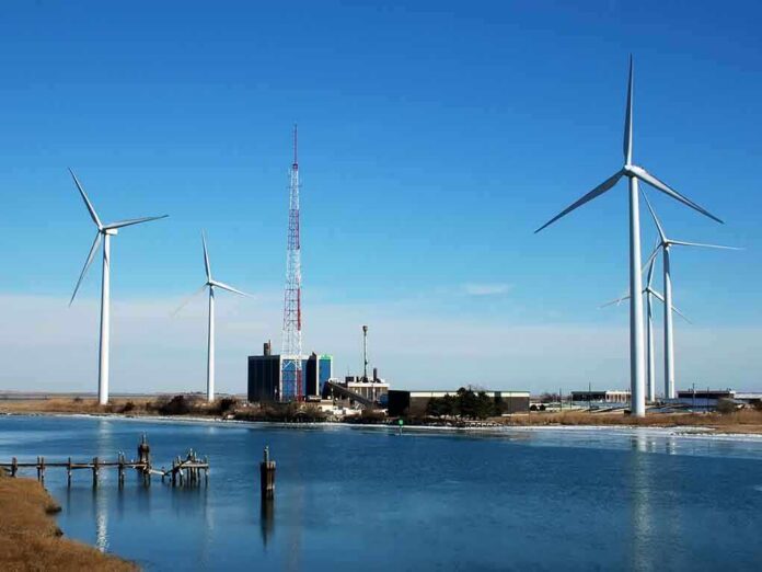 Wind turbines and a communication tower near a body of water under a clear blue sky