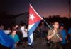 A group of people participating in a protest march holding a Cuban flag