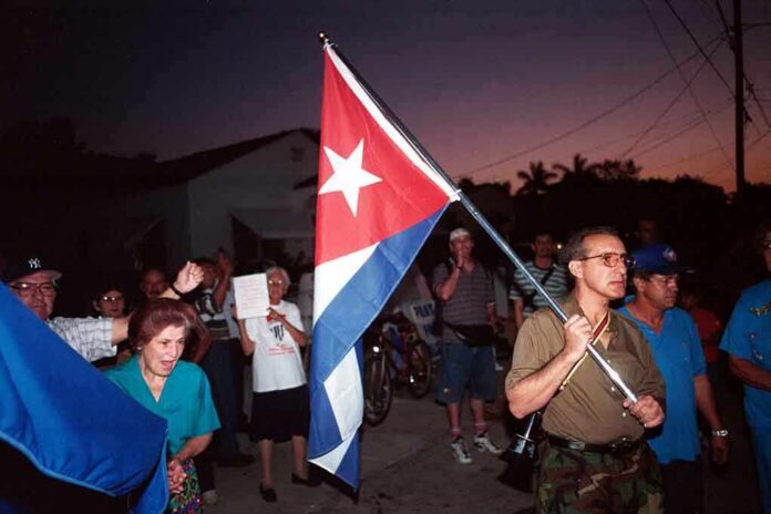 A group of people participating in a protest march holding a Cuban flag