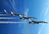 Four military jets flying in formation against a blue sky, leaving smoke trails