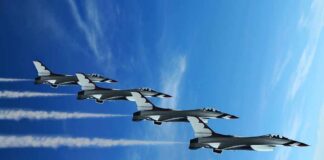 Four military jets flying in formation against a blue sky, leaving smoke trails