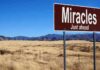 A road sign reading 'Miracles Just ahead' in a desert landscape