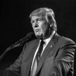 A public figure speaking into a microphone in a serious manner