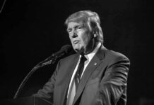 A public figure speaking into a microphone in a serious manner