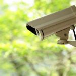 Ring Camera UNEXPECTEDLY TURNED His Life AROUND A security camera mounted outdoors with a blurred green background