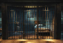 Empty prison cell with metal bars and bed.