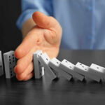 ESSENTIAL Chemical Chokehold THREATENS MINING Hand stopping falling row of dominoes.