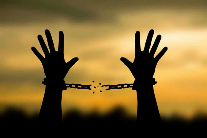 Hands breaking free from chains at sunset.