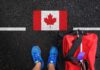 A person's feet next to a red backpack on a road with a Canadian flag painted on it