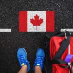 A person's feet next to a red backpack on a road with a Canadian flag painted on it