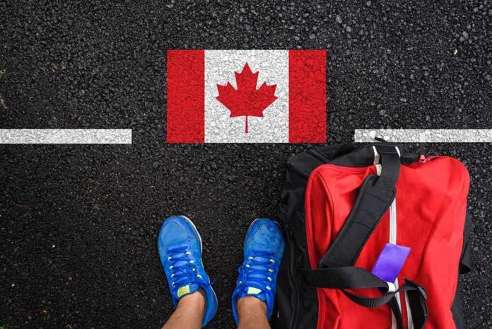 A person's feet next to a red backpack on a road with a Canadian flag painted on it