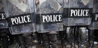 Police officers in riot gear standing behind shields marked POLICE