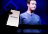 A hand holding a smartphone displaying the Meta logo with a blurred figure in the background
