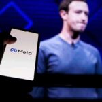 A hand holding a smartphone displaying the Meta logo with a blurred figure in the background