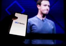 A hand holding a smartphone displaying the Meta logo with a blurred figure in the background