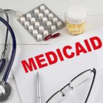 Medical documents with the word Medicaid prominently displayed alongside a stethoscope and medication