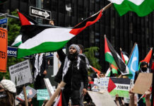 Protesters with flags and signs, one holding a megaphone.