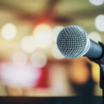 MUSIC INDUSTRY SHAKEN: Face’s Triple Threat! Microphone with blurred lights in the background.