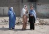 Three women in traditional attire standing in an urban setting with debris in the background