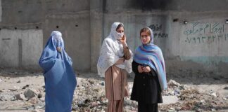 Three women in traditional attire standing in an urban setting with debris in the background