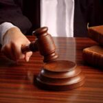 TRUMP’S $83M PAYMENT Paused! A judges hand holding a gavel over a wooden desk with law books