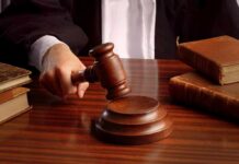 TRUMP’S $83M PAYMENT Paused! A judges hand holding a gavel over a wooden desk with law books
