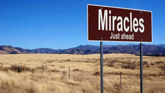 shutterstock_429570871-1 A road sign reading 'Miracles Just ahead' in a desert landscape