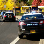 Lawsuit Targets Secret Service After Butler Rally Shooting Police cars and school buses on a road.