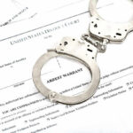 9–0 SMACKDOWN: Court Pushes Back Against Federal Case Handcuffs on top of an arrest warrant document.