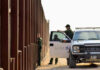 Cartel Tunnel Hides Under U.S. Storefront Border patrol agents near a tall metal fence.