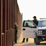 Cartel Tunnel Hides Under U.S. Storefront Border patrol agents near a tall metal fence.