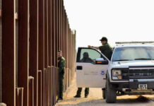Cartel Tunnel Hides Under U.S. Storefront Border patrol agents near a tall metal fence.