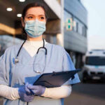 Doctor Brings Ebola Home — Paris On Edge Nurse in scrubs and mask outside hospital holding clipboard.