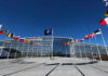 Belarus Becomes Russia’s Forward Base Flags outside NATO headquarters building under clear blue sky.