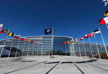 Belarus Becomes Russia’s Forward Base Flags outside NATO headquarters building under clear blue sky.