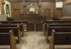 Pleads Guilty: From Insider to Defendant Interior view of an empty courtroom with wooden benches and a judges bench