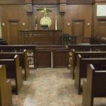 Pleads Guilty: From Insider to Defendant Interior view of an empty courtroom with wooden benches and a judges bench