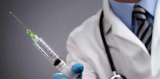 A doctor holding a syringe with a stethoscope around their neck