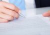 A hand holding a pen poised above a document for signing