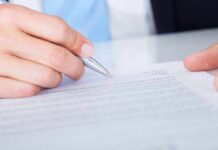 DOJ Indicts SPLC Over Alleged Fraud and Hidden Transfers A hand holding a pen poised above a document for signing