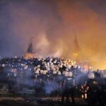 Turkey Locks Down Capital Before NATO Leaders Arrive A large crowd of police officers in helmets facing a smoky protest scene at night